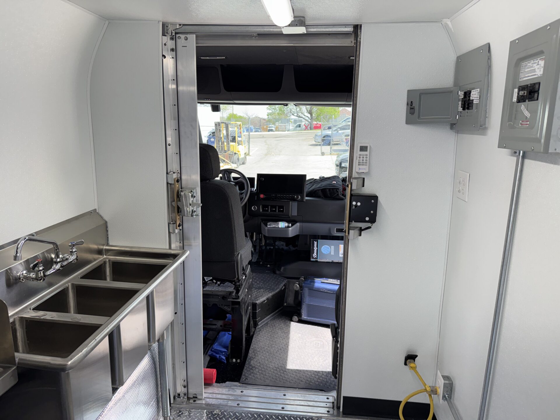 Interior of the BrightDrop Crumbl Cookie food truck looking forward through the bulkhead to the driver cab, showing the dual breaker panels and shore power connection