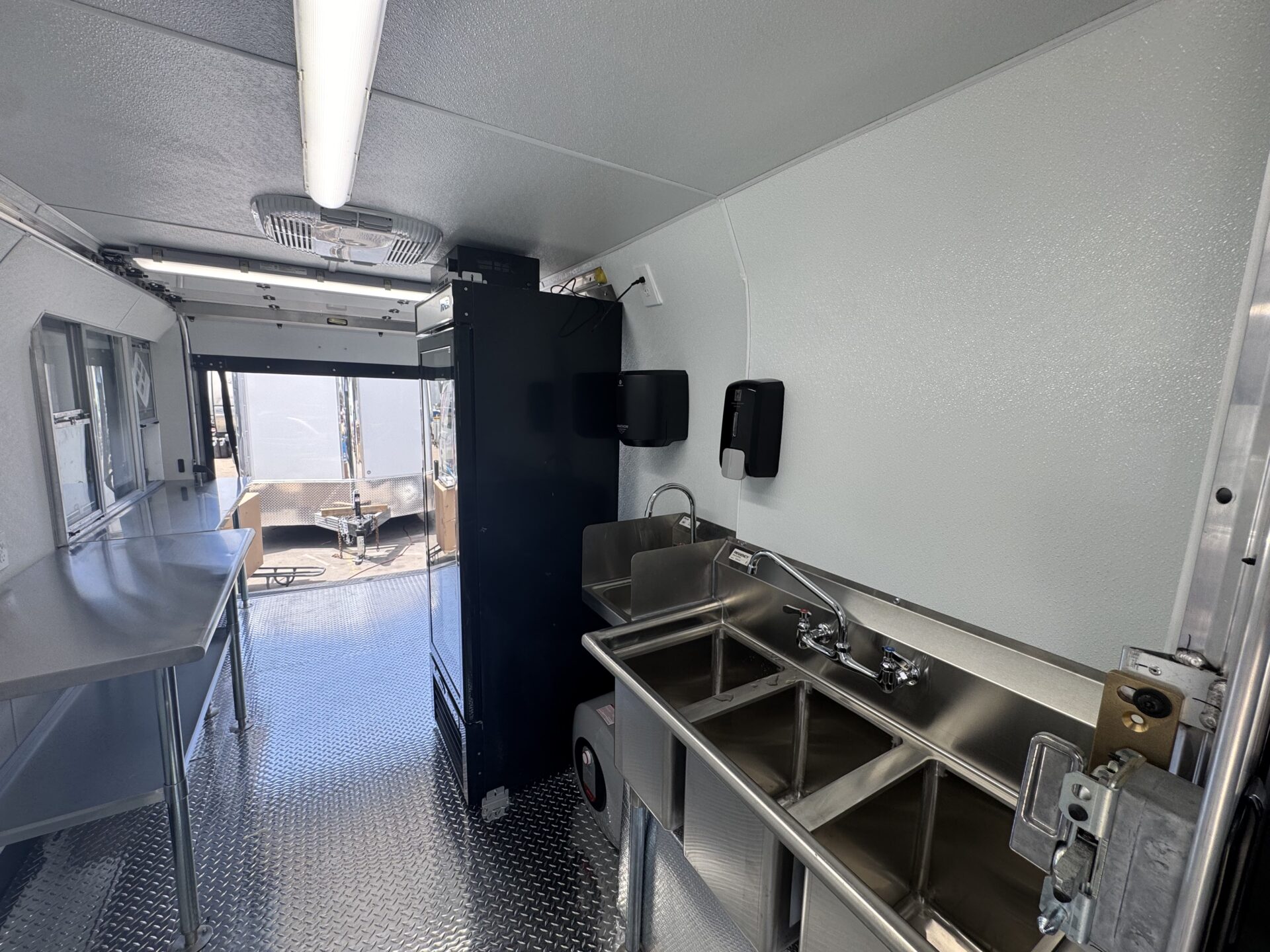 Three compartment sink and hand wash sink with soap and paper towel dispensers inside the Crumbl Cookie food truck