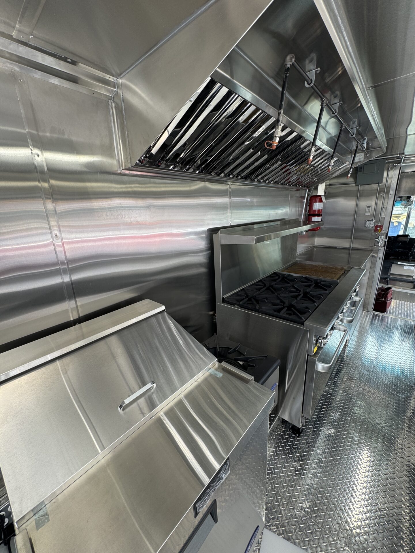 Stainless steel cooking line with six burner range, griddle and Type I hood on a Wichita food truck build
