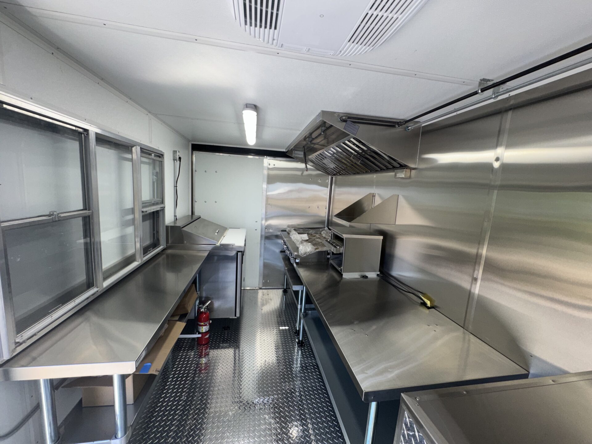 Interior of the bagel food trailer showing the stainless steel cooking wall with the LP griddle and conveyor oven under the hood vent