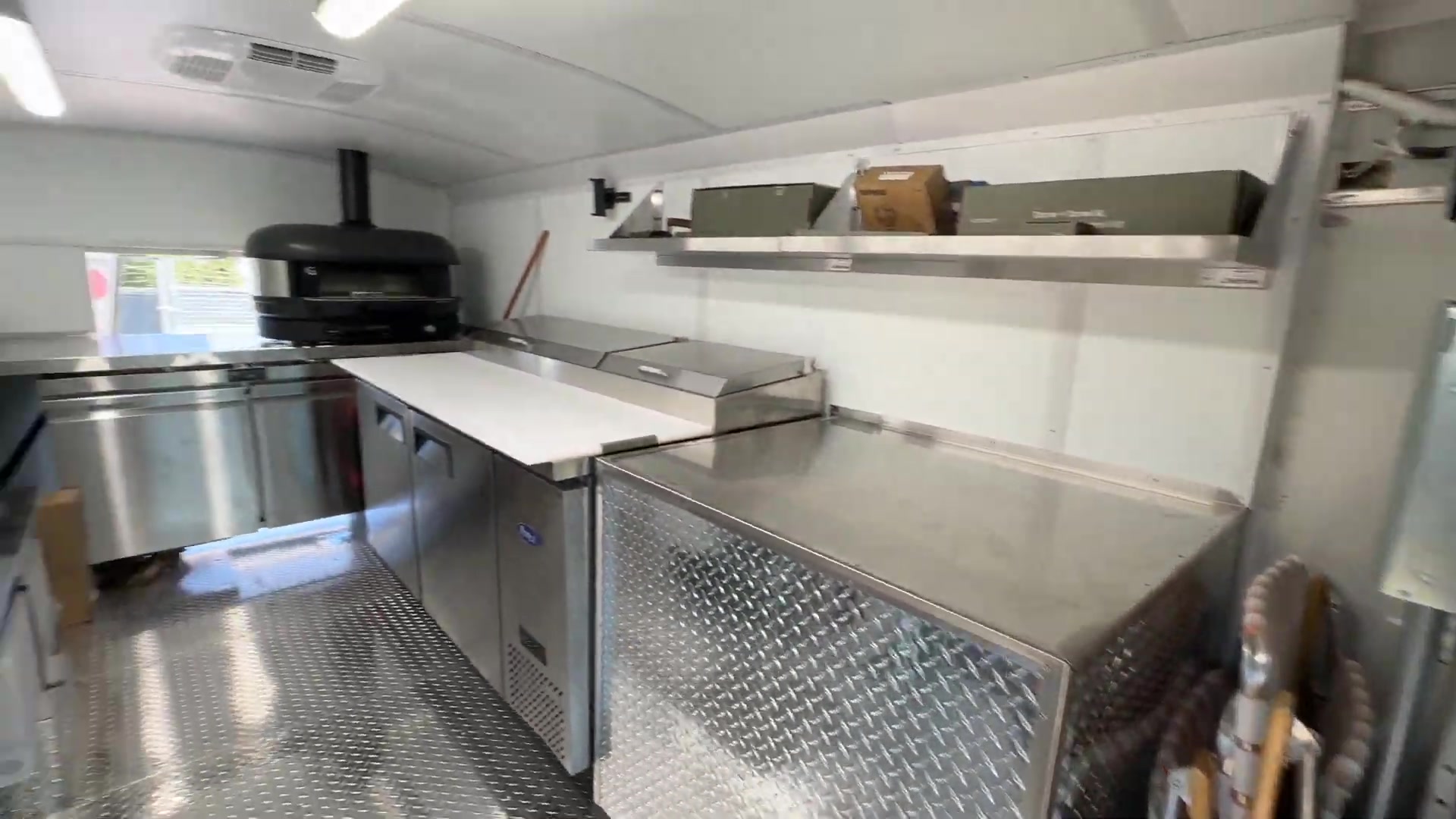 Interior of the 14ft pizza bus with the oven at the far end, prep table, worktop refrigerator and wall shelves