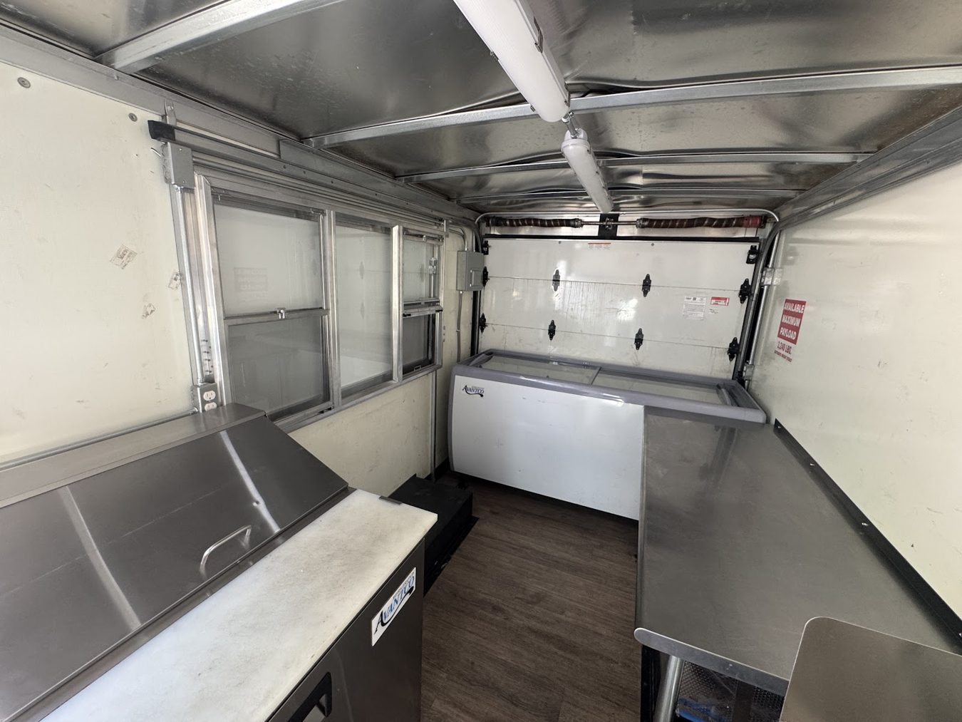 Interior of the açaí bowl food truck seen from the rear doors with the freezer, tables and window