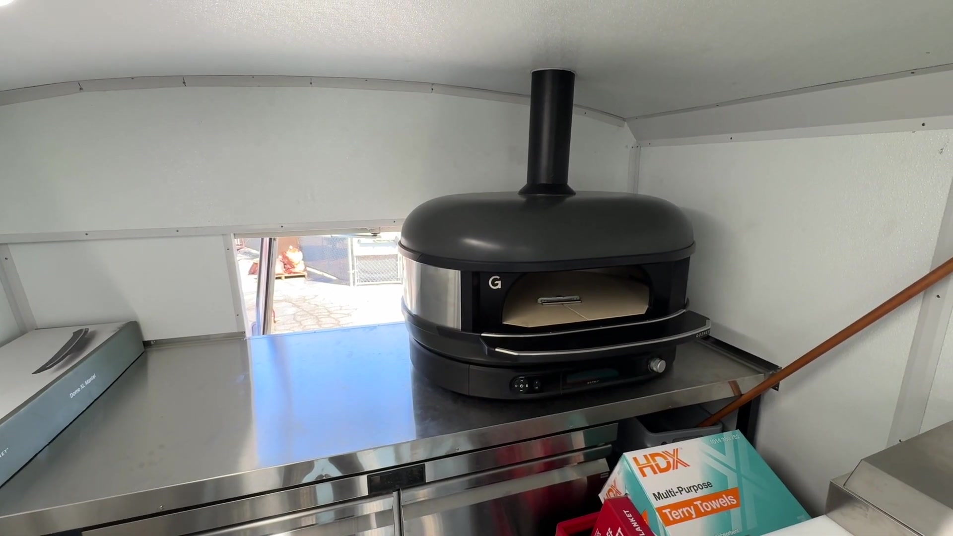 Gozney dome pizza oven with its own chimney on a stainless worktop refrigerator inside the food bus