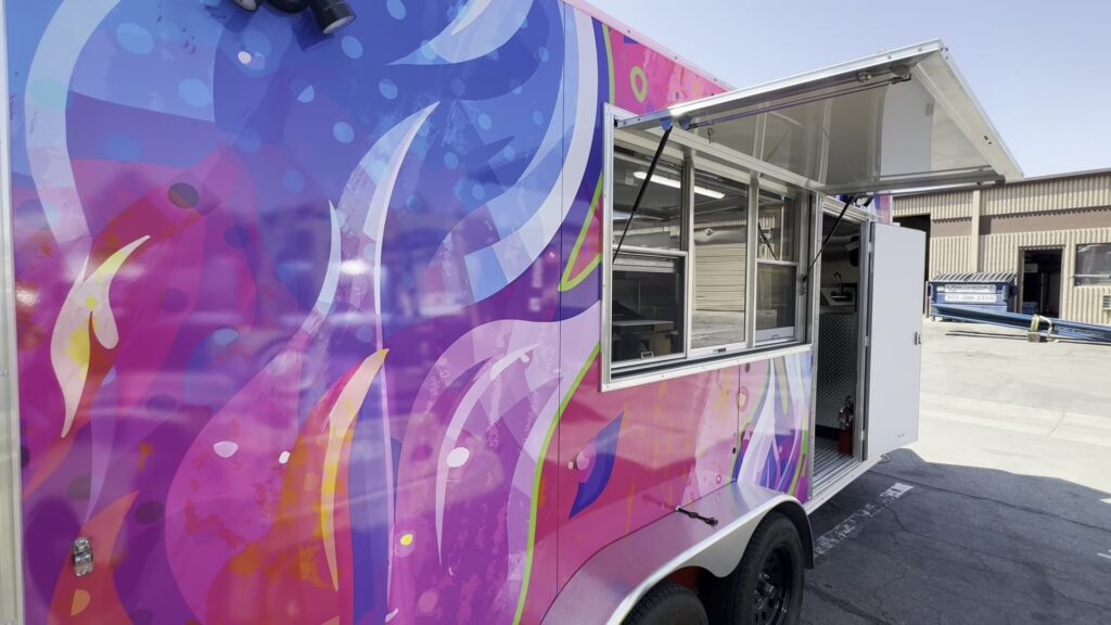 16ft Sizzlin Street Bites food trailer in a pink and purple wrap with the service window open, built for Longmont, Colorado