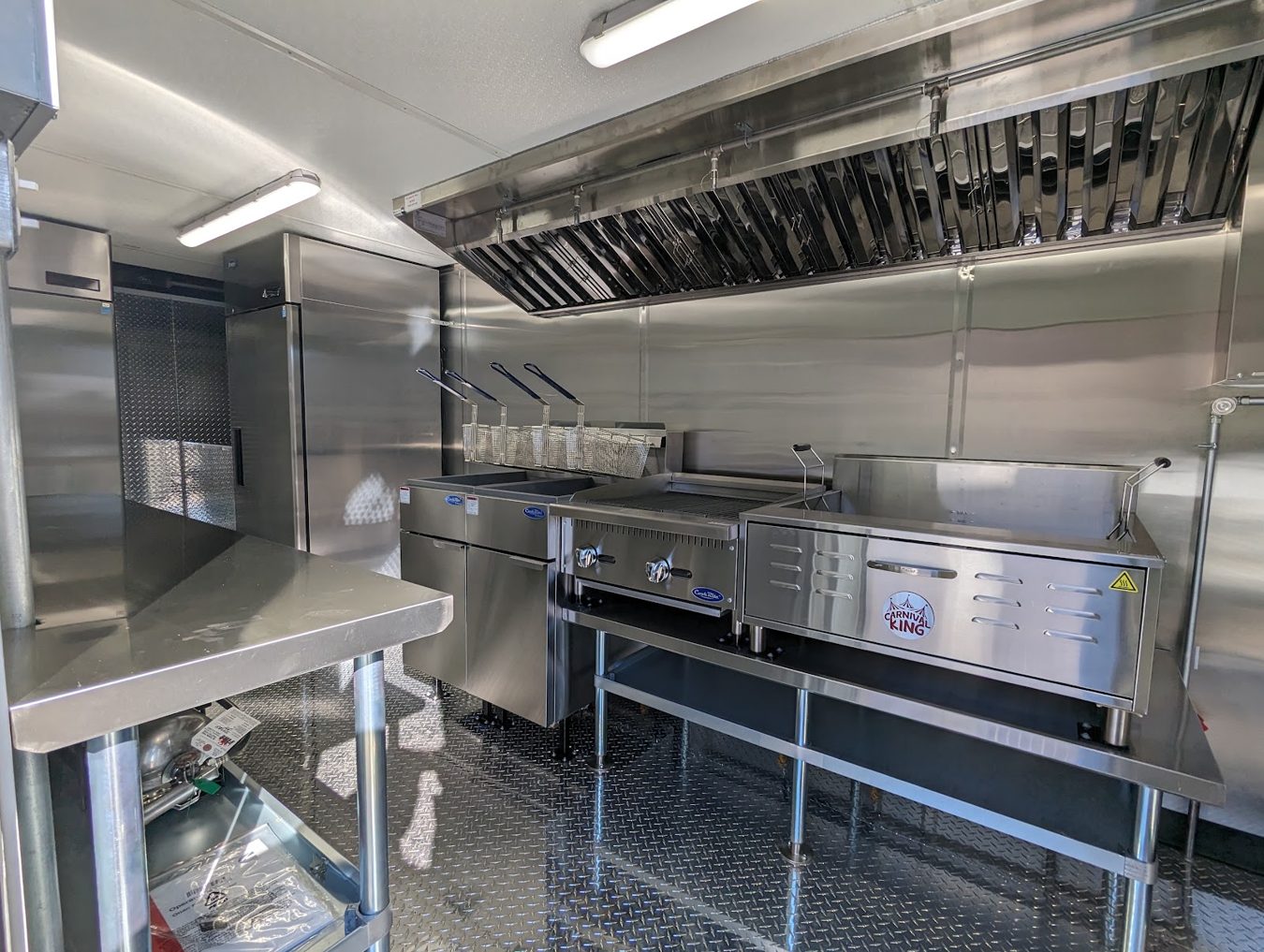 Fryer line inside the tempura trailer with two forty pound fryers, a charbroiler and a flat bottom fryer under the eight foot hood